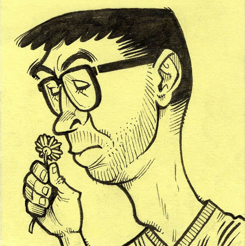 Man with glasses smelling a small flower